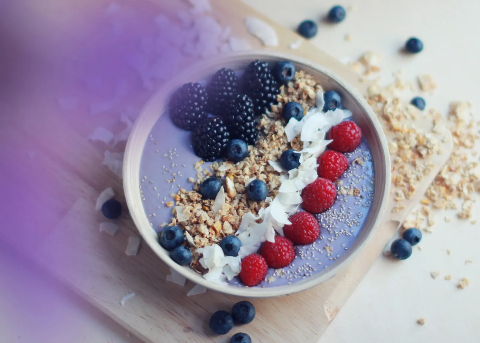 Tigela de açaí com granola, coco ralado, amora, mirtilo e framboesa sobre uma tábua de madeira
