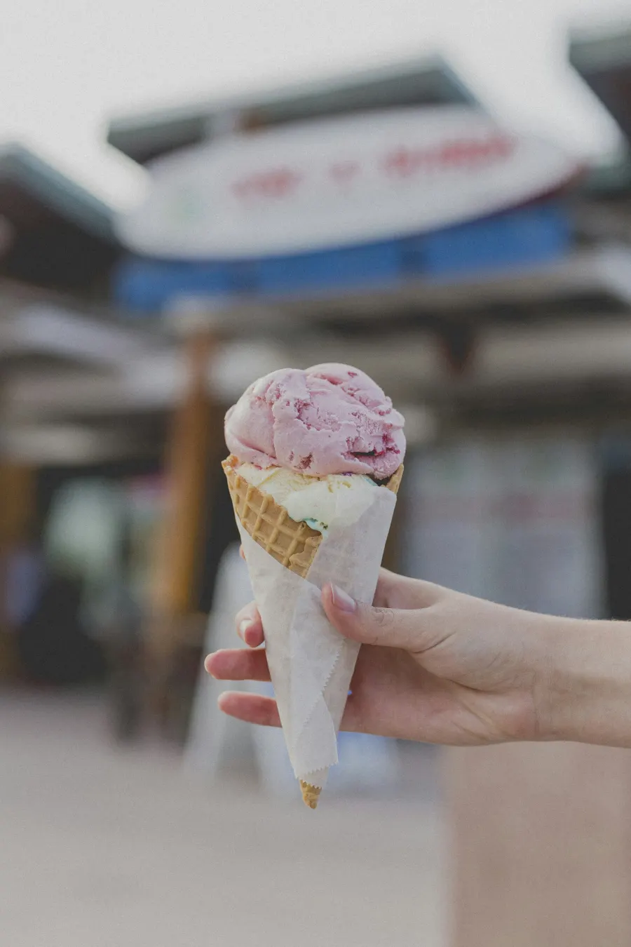 Mão segurando casquinha com uma bola de sorvete rosa sobre uma de creme