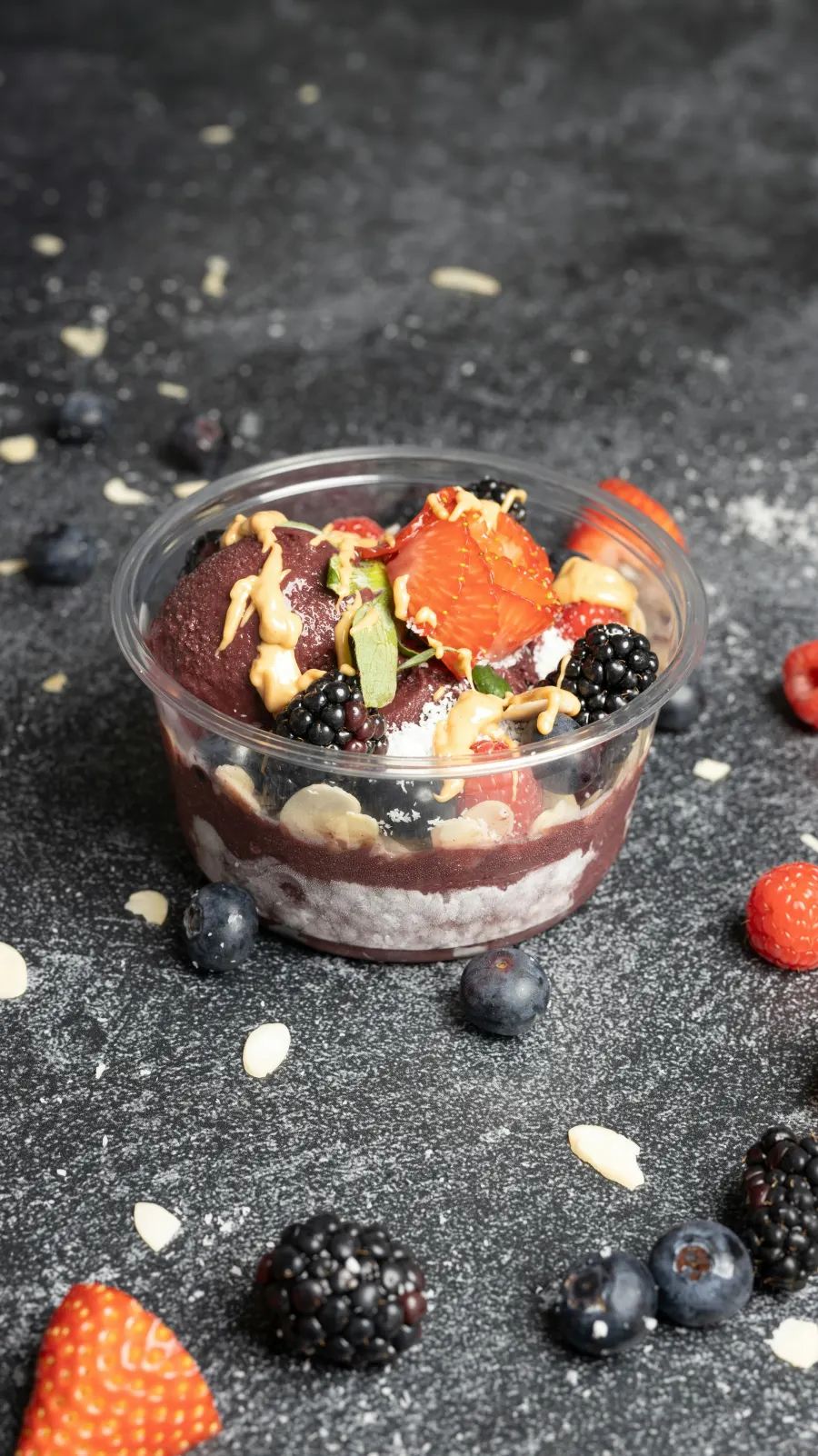 Pote transparente de açaí em camadas com morango, amora e calda de amendoim