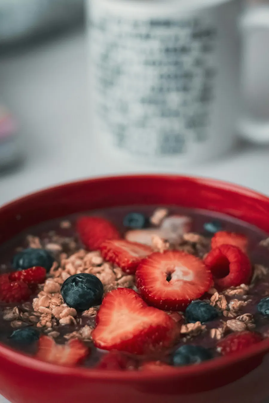 Tigela vermelha de açaí com granola, morango fatiado, framboesa e mirtilo