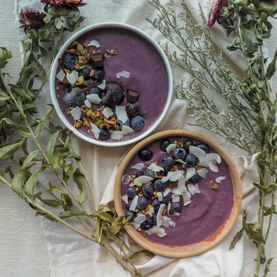 Duas tigelas de açaí com granola, coco em lascas e mirtilo sobre toalha