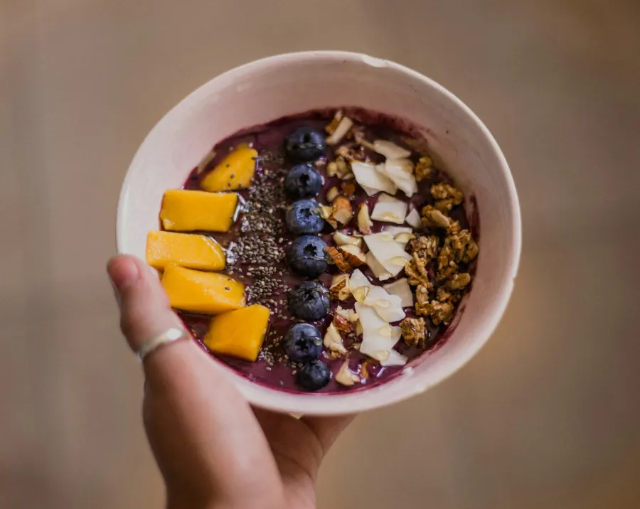 Mão segurando tigela de açaí com manga, mirtilo e lascas de amêndoa