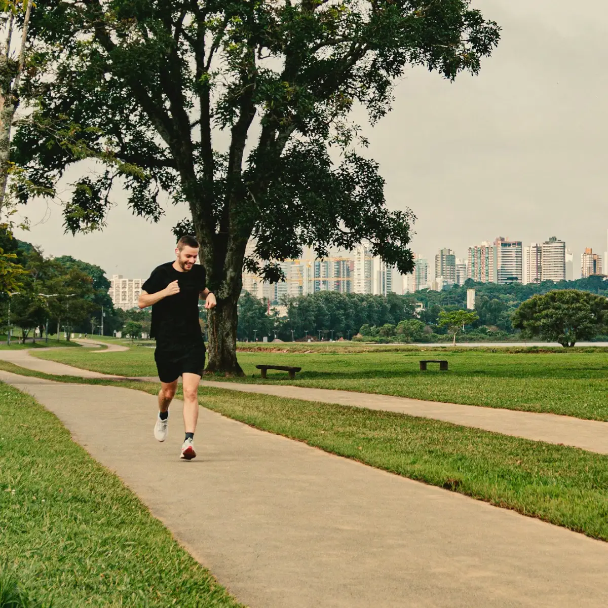 Aluno correndo sozinho na pista de um parque, com um lago e prédios ao fundo