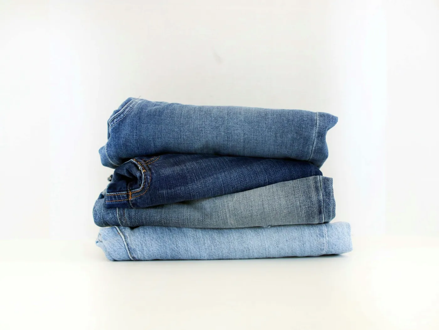 Pilha de quatro calças jeans dobradas, em tons de azul