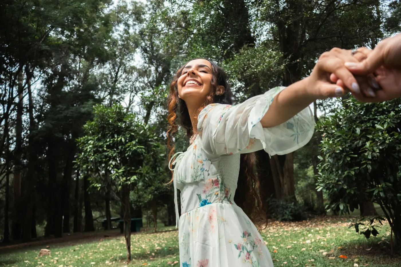 Mulher sorrindo num parque, de vestido branco com flores e manga bufante de tule