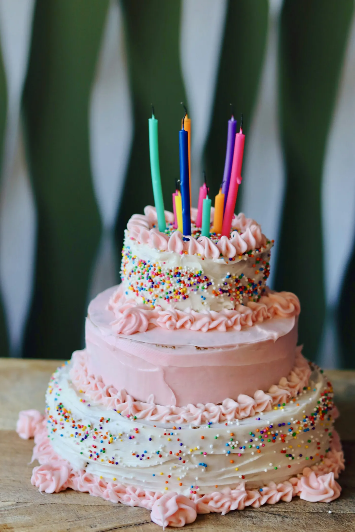 Bolo de dois andares cobertos de chantilly rosa e granulado, com velas coloridas no topo