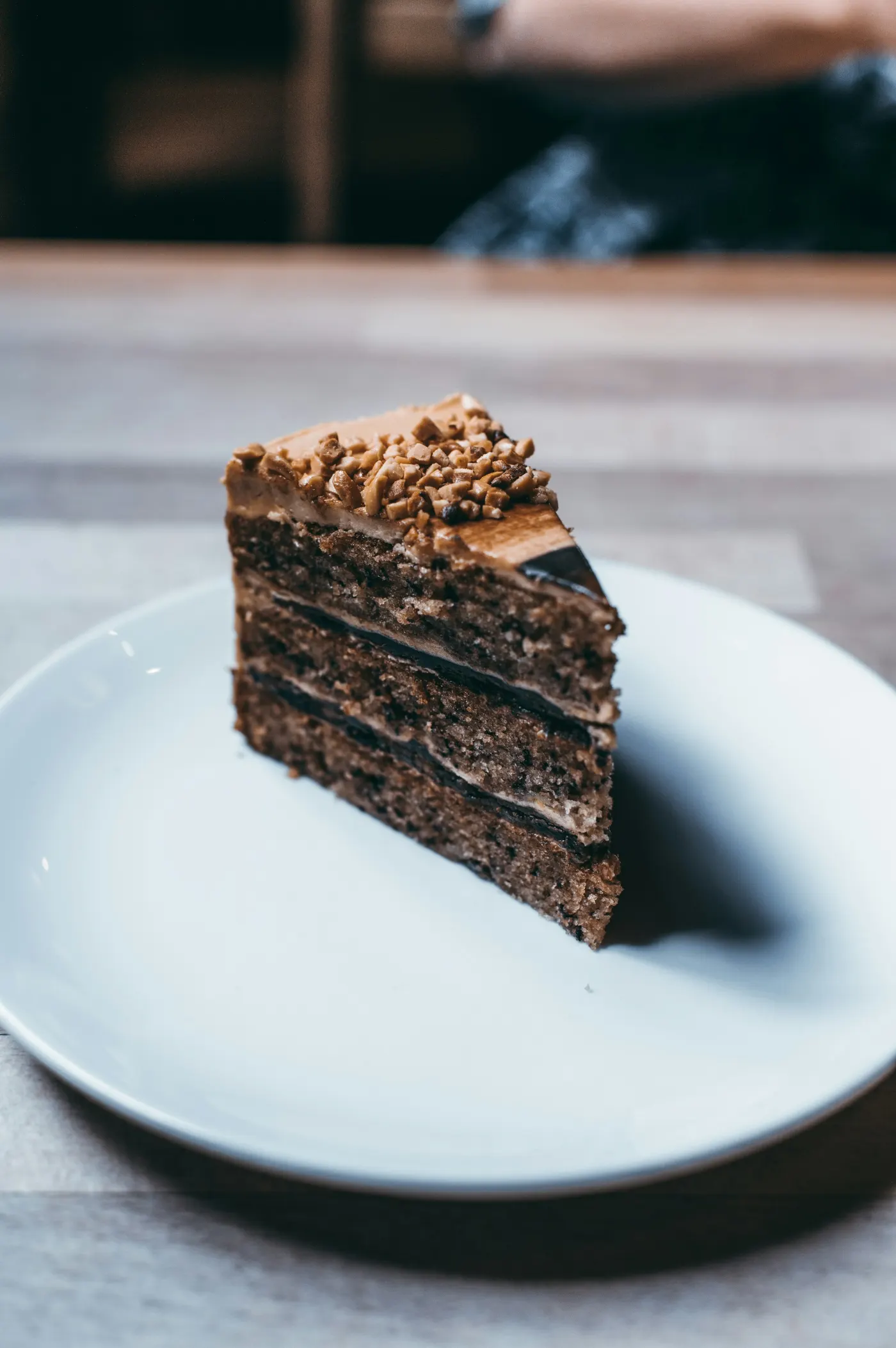 Fatia de bolo de chocolate com três camadas de massa, recheio de brigadeiro e paçoca por cima, num prato branco sobre a mesa de madeira