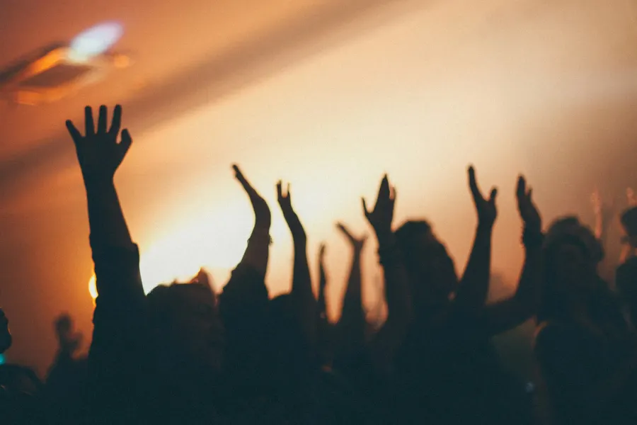 Silhueta de mãos erguidas durante o louvor, contra a luz quente do palco