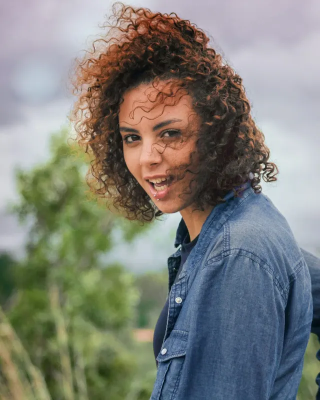 Isabela Nunes, de cabelo cacheado e camisa jeans, ao ar livre