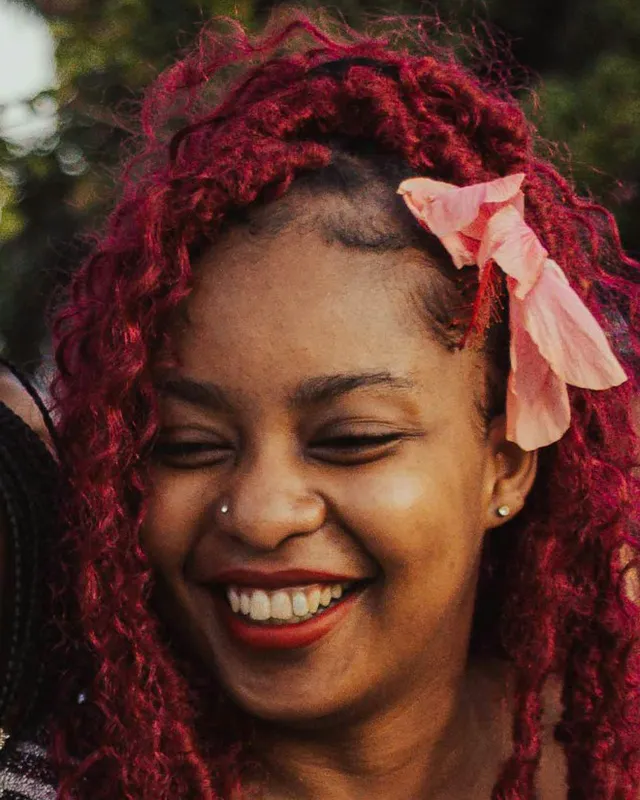 Marina Sales, de cabelo cacheado vermelho e laço rosa, sorrindo