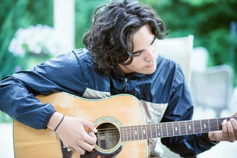 Rapaz de cabelo ondulado tocando violão