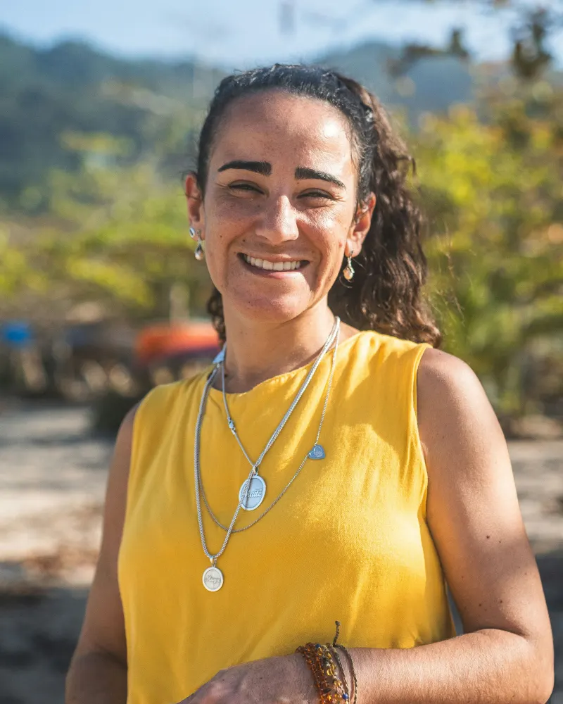 Helena Bastos, de camiseta amarela, sorrindo ao ar livre