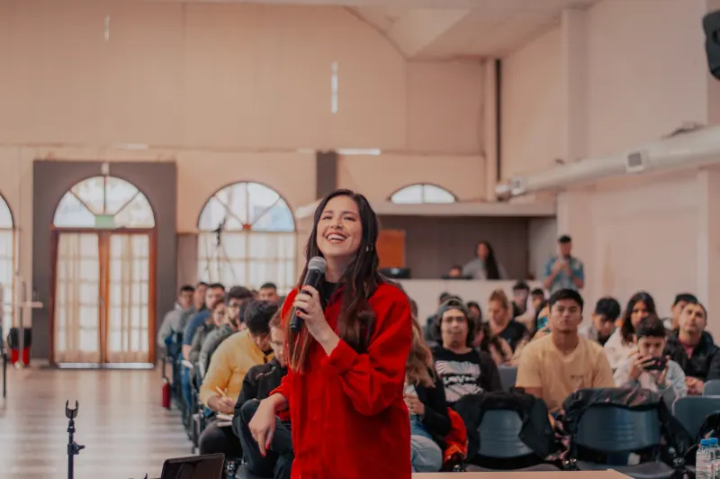 Marta Nogueira, de blusa vermelha, com o microfone na mão diante da plateia
