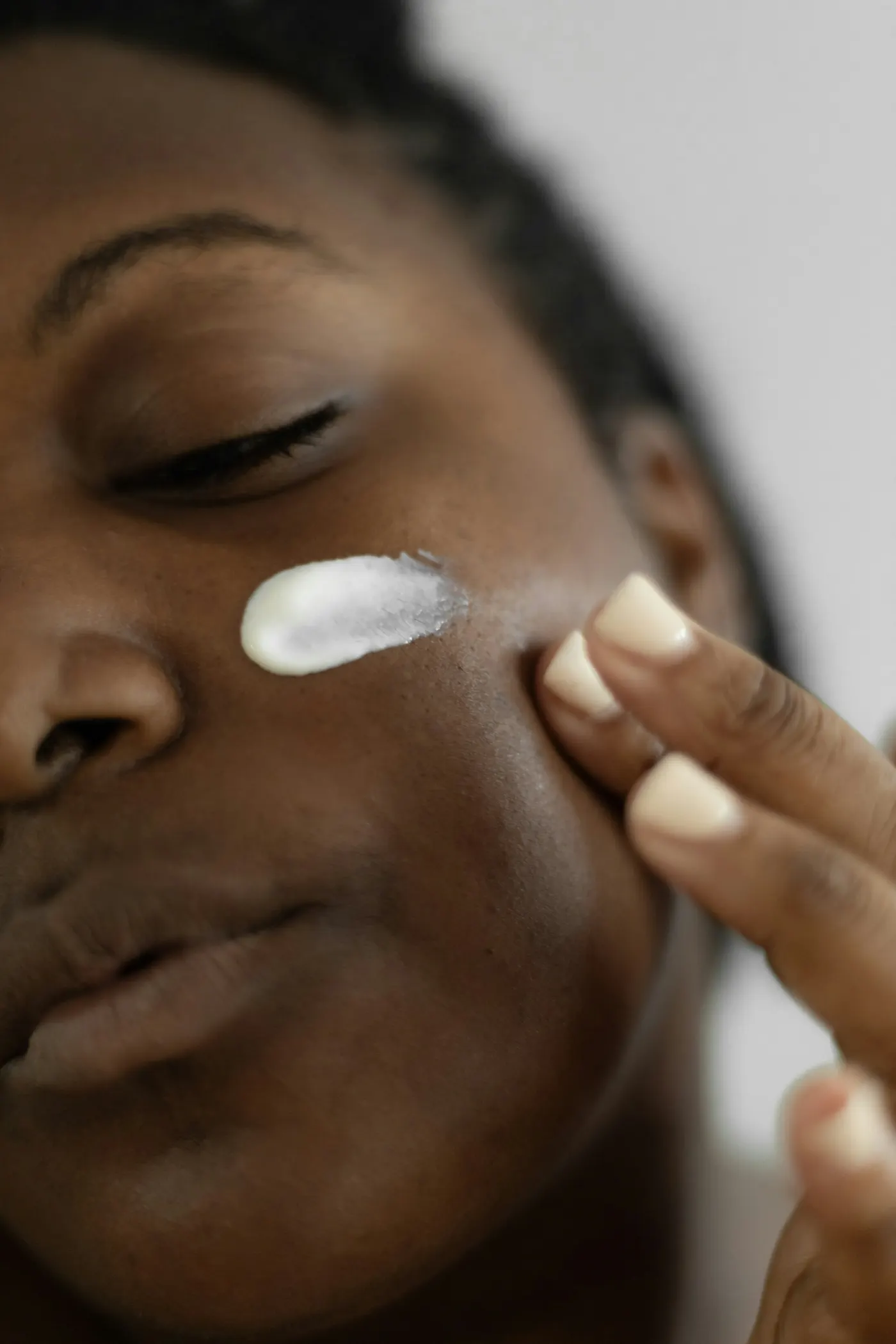 Rosto de mulher de pele escura, de olhos fechados, com creme branco passado na bochecha