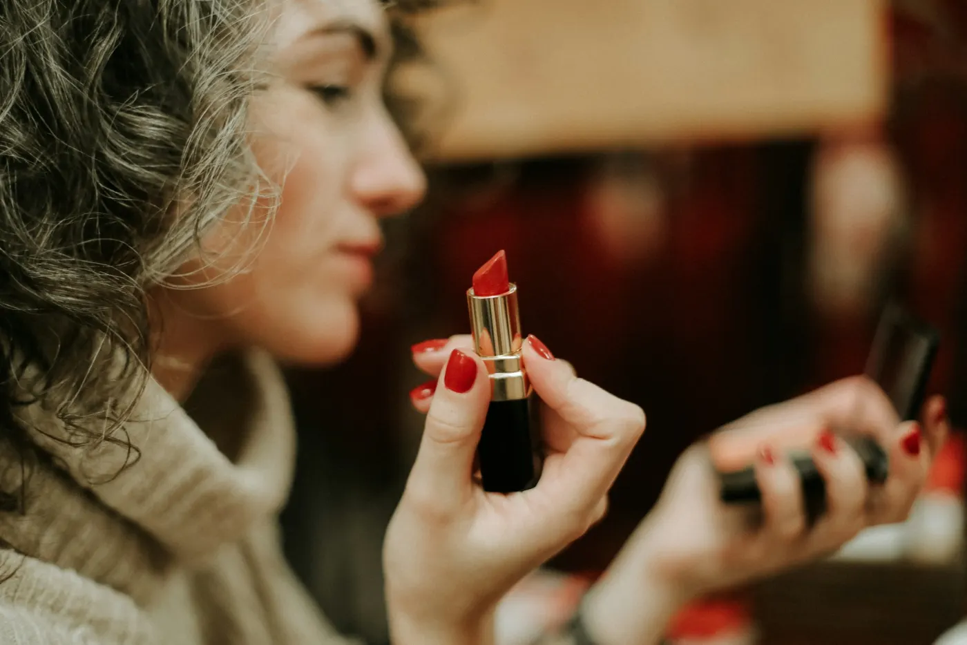 Mulher de suéter segurando um batom vermelho diante do espelho