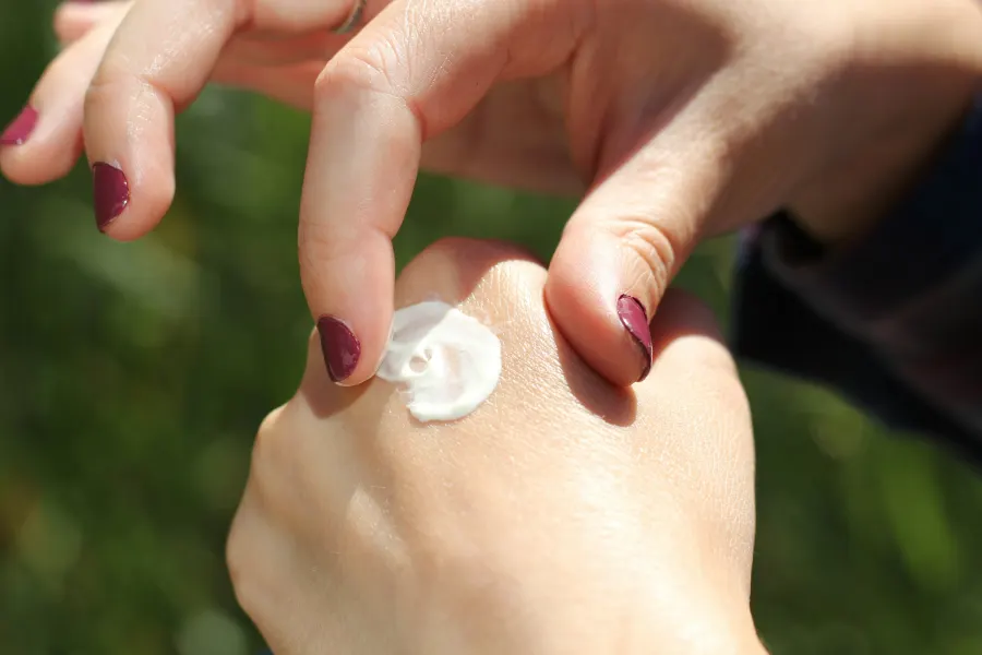Mão com esmalte vinho recebendo uma porção de creme branco