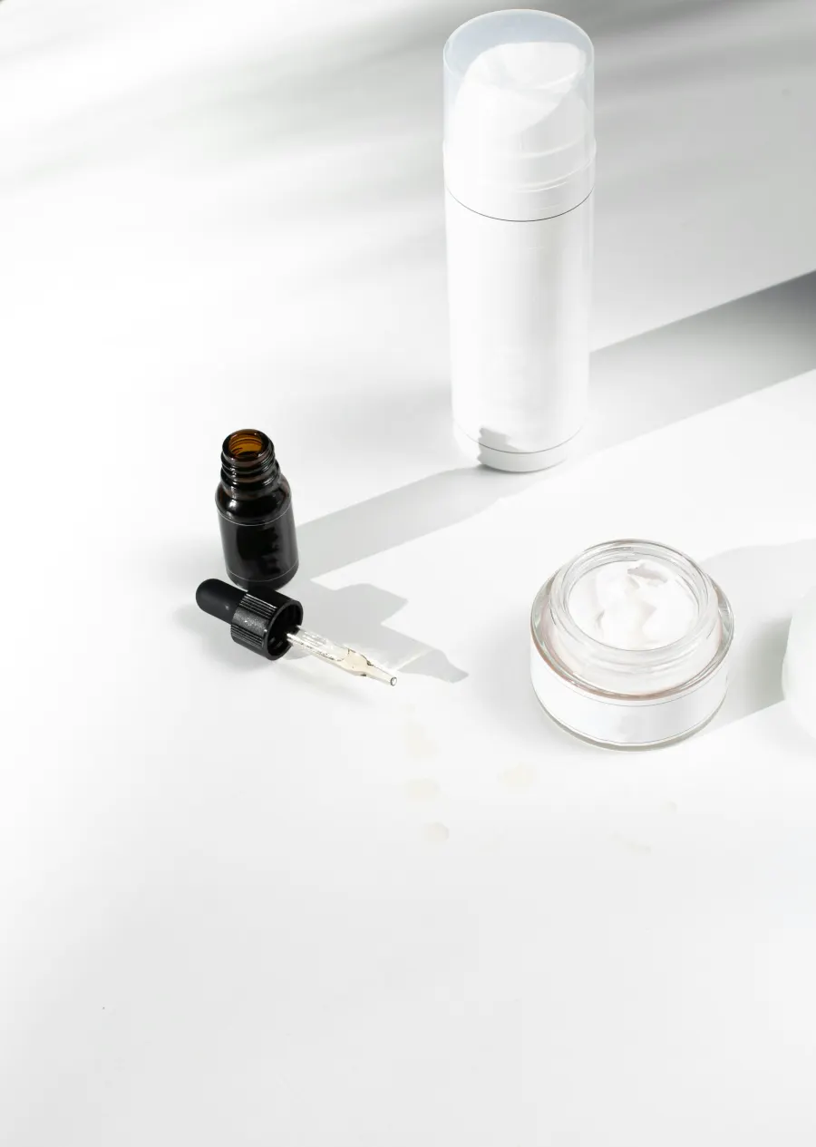 Frasco branco, conta-gotas preto e pote de creme sobre superfície branca