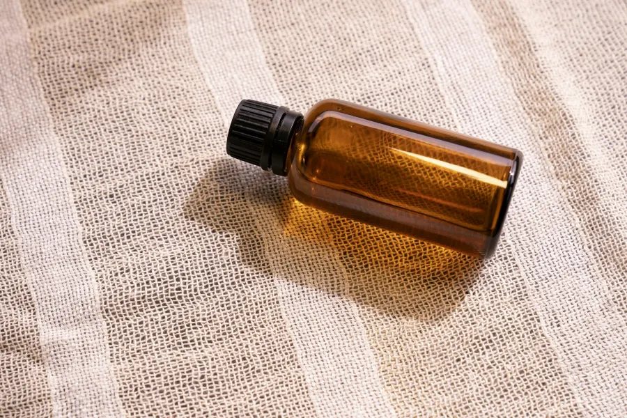 Frasco âmbar de óleo com tampa preta deitado sobre um tecido de gaze clara