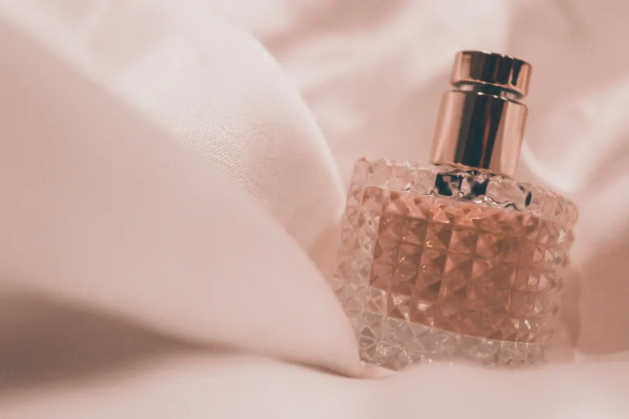 Frasco de perfume rosa de vidro facetado sobre um tecido claro