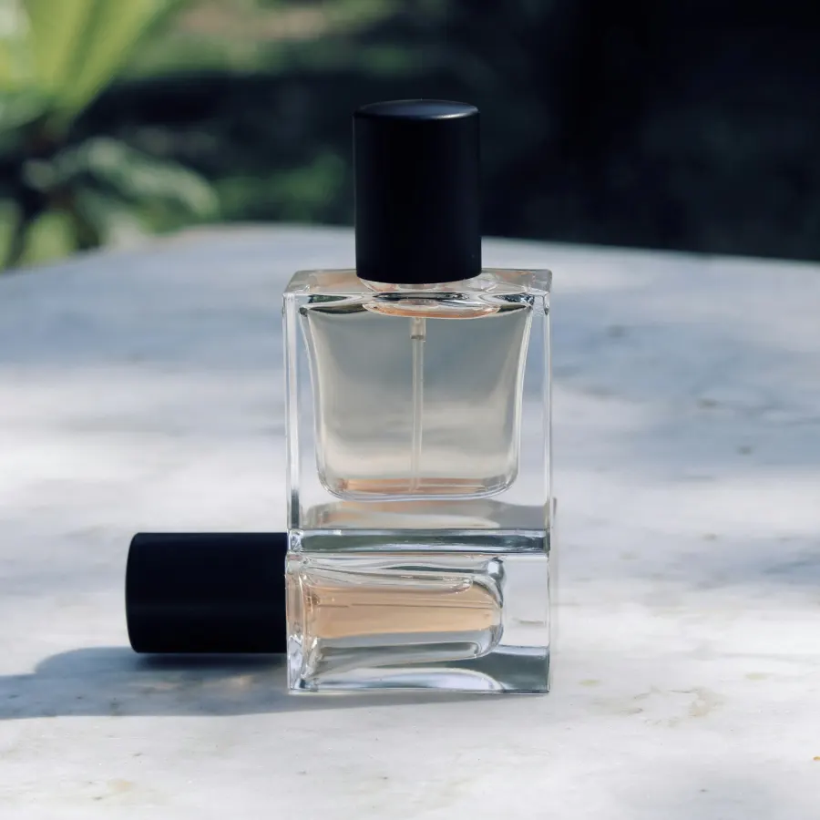 Frasco de perfume de vidro transparente com tampa preta sobre uma mesa de pedra clara