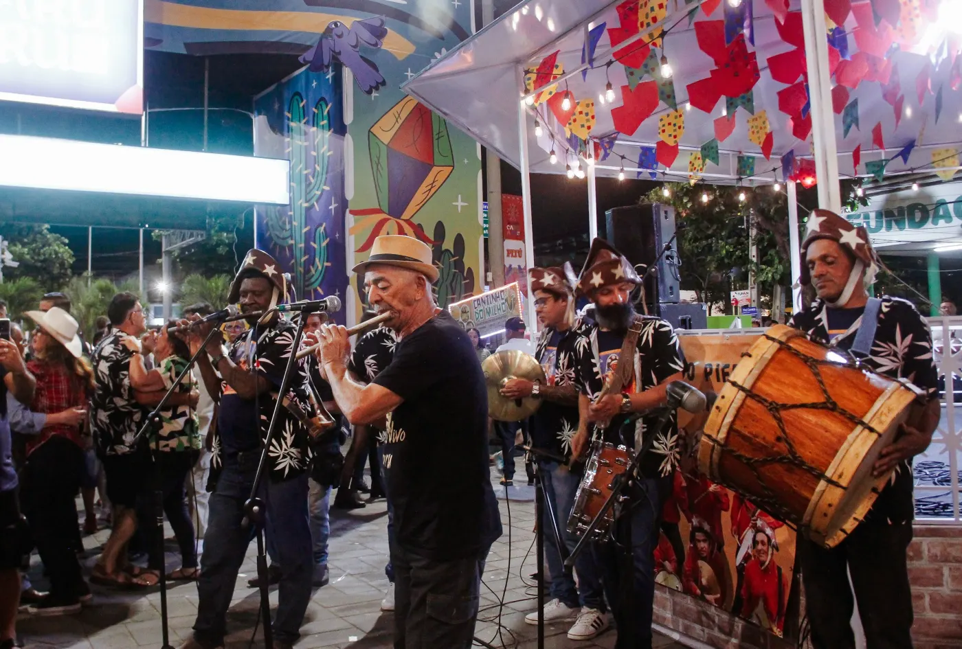 Banda de forró tocando numa rua enfeitada com bandeirinhas e luzes de cordão