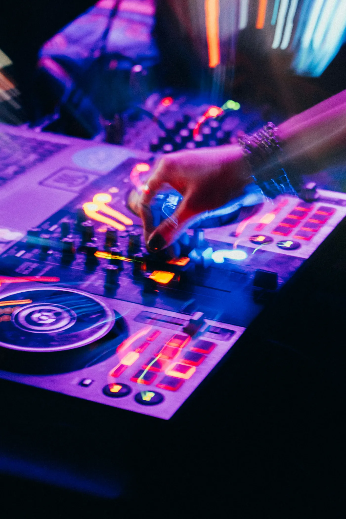 Mão do DJ sobre uma controladora com botões acesos em roxo e laranja
