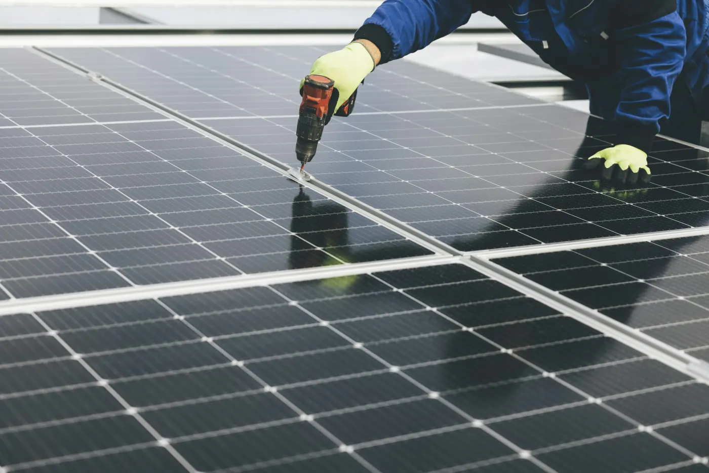 Técnico de luva e macacão azul aparafusando a fixação de um painel solar
