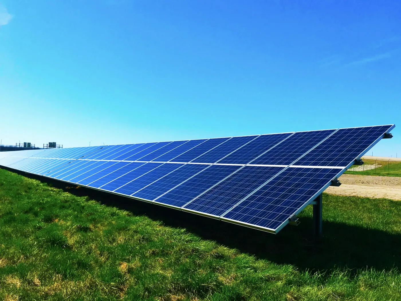 Fileira de painéis solares montada no chão, sobre o capim, em dia de céu aberto