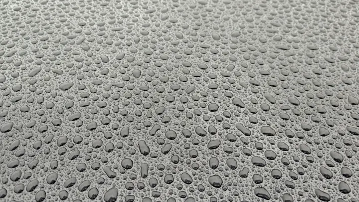Gotas de água em formato de pérola sobre a pintura cinza de um carro encerado