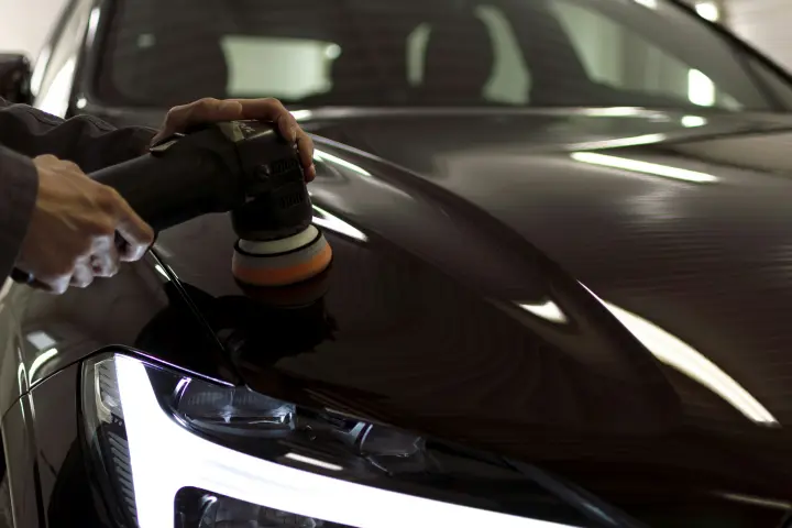 Politriz passando no capô escuro de um carro, com o brilho do farol no canto