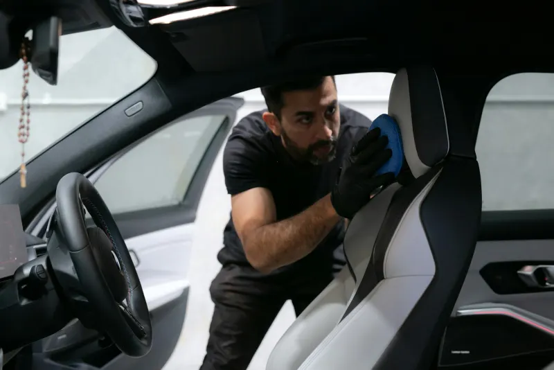 Wesley passando o pano de microfibra no banco de um carro, de dentro da porta aberta