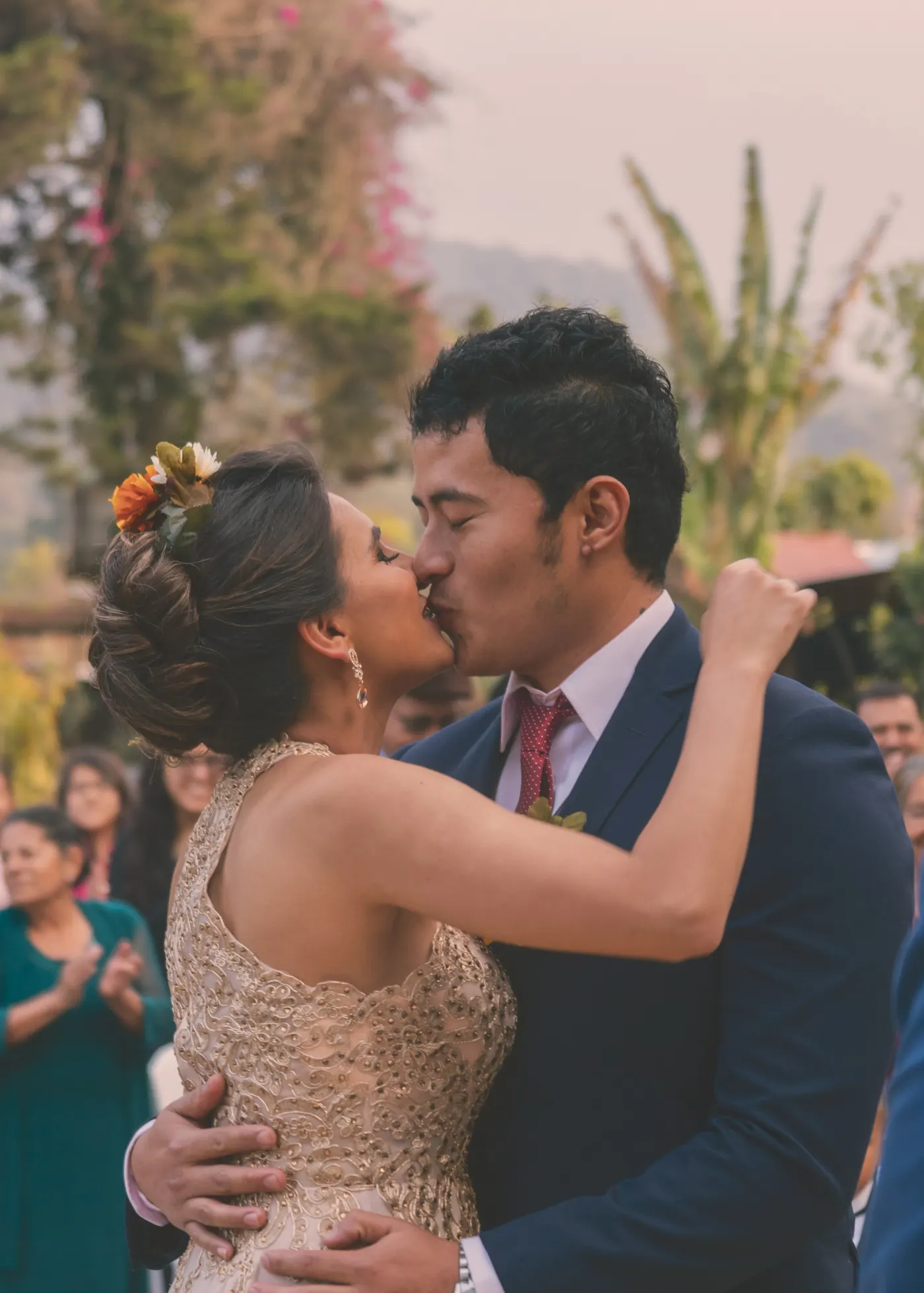 Noivos se beijando durante a festa, com convidados aplaudindo ao fundo