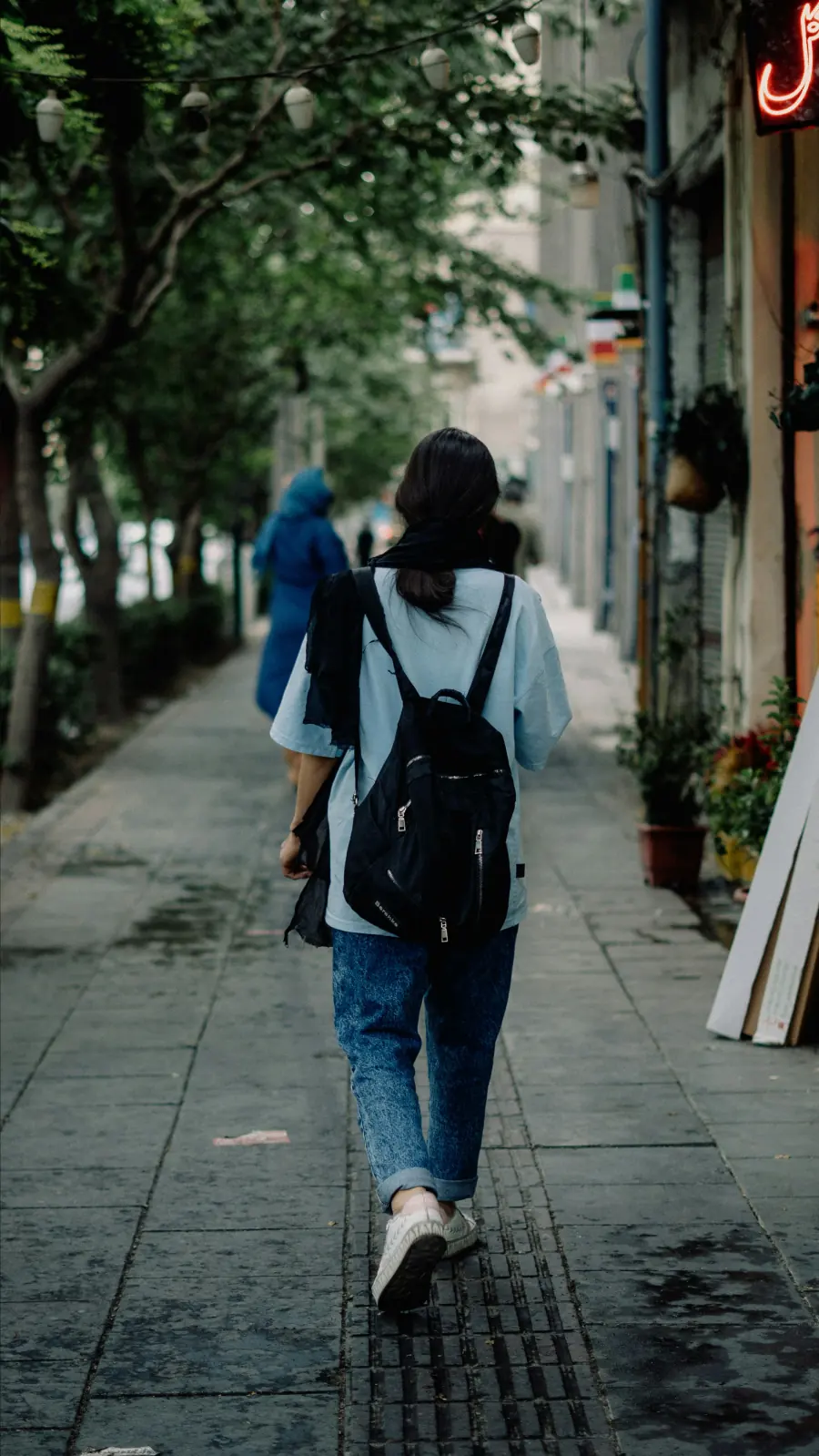 Moça de costas andando na rua com mochila preta