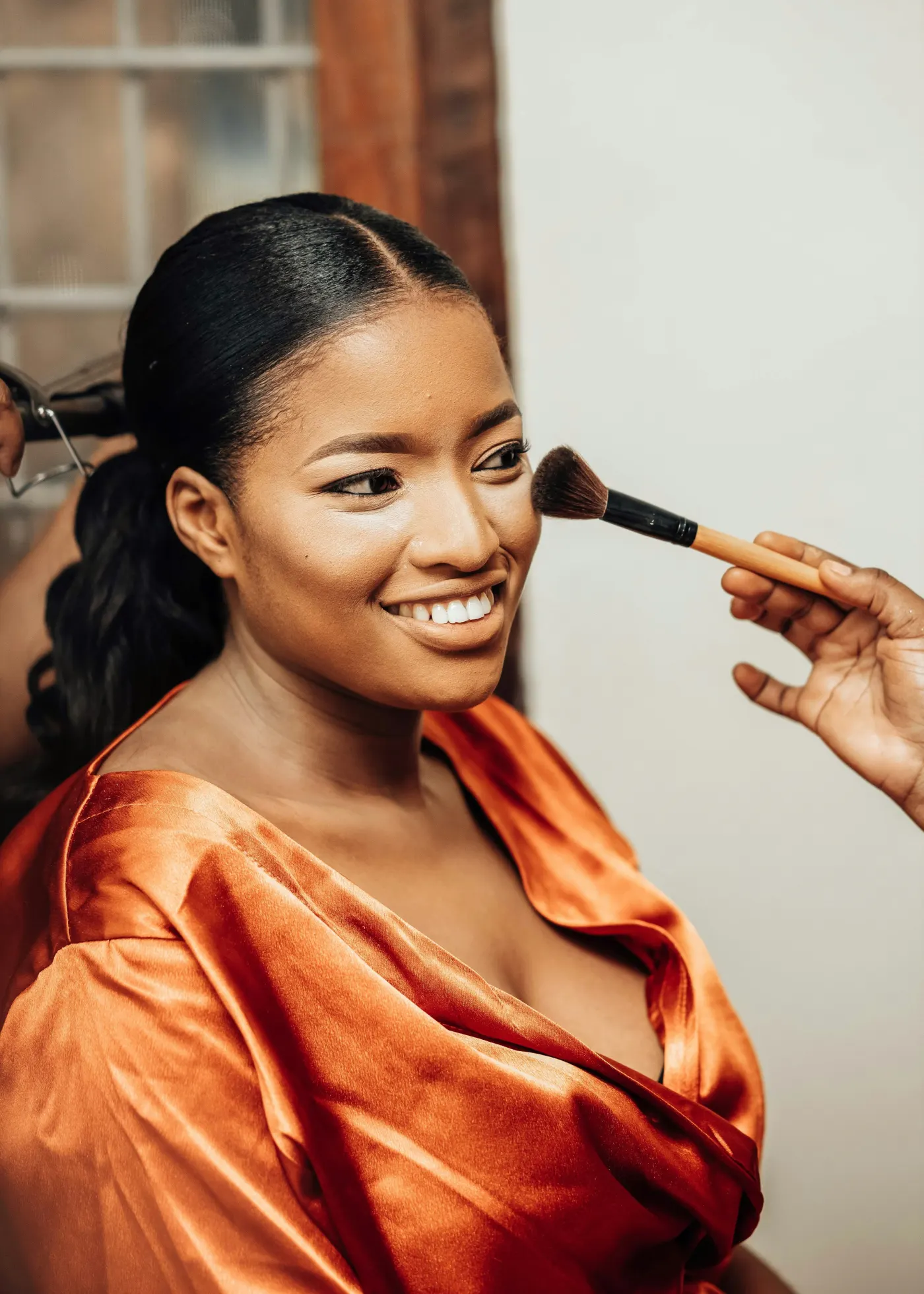 Mulher de roupão cor de telha sorrindo enquanto recebe blush com um pincel