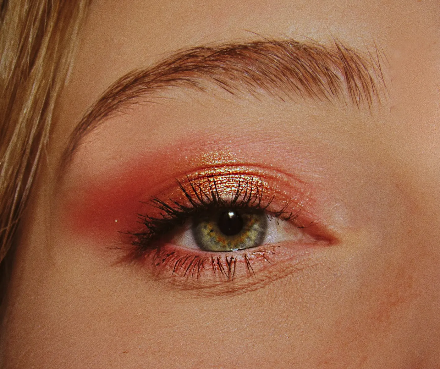 Olho com sombra coral e dourada e cílios marcados, em close