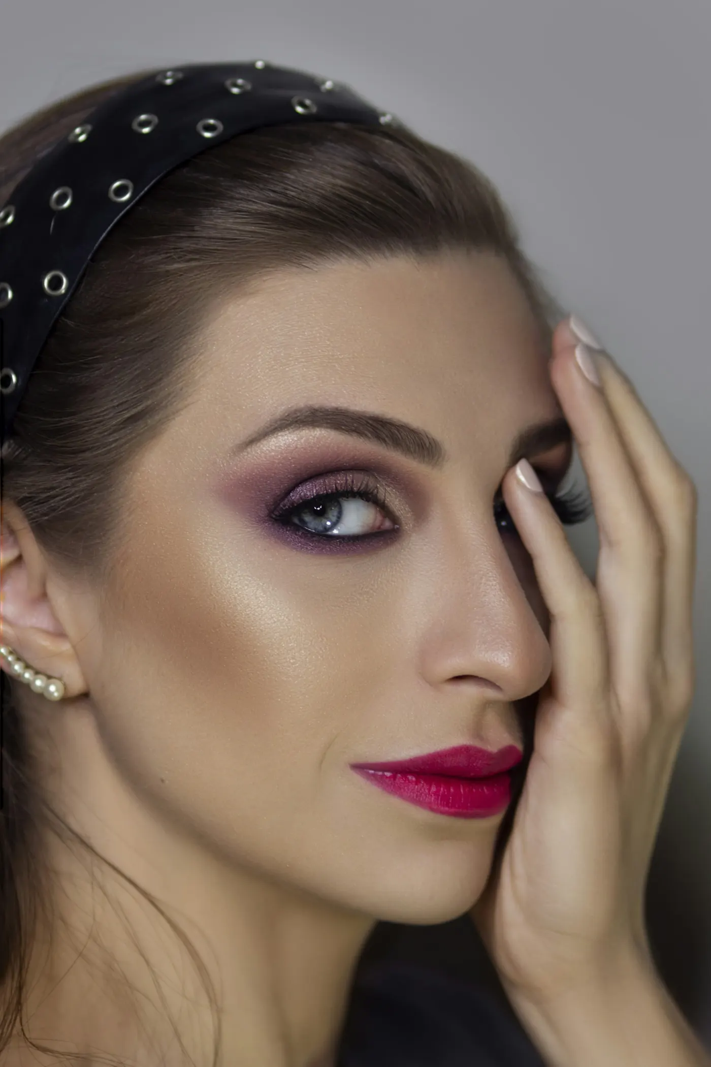 Mulher com batom pink e sombra ameixa, a mão no rosto
