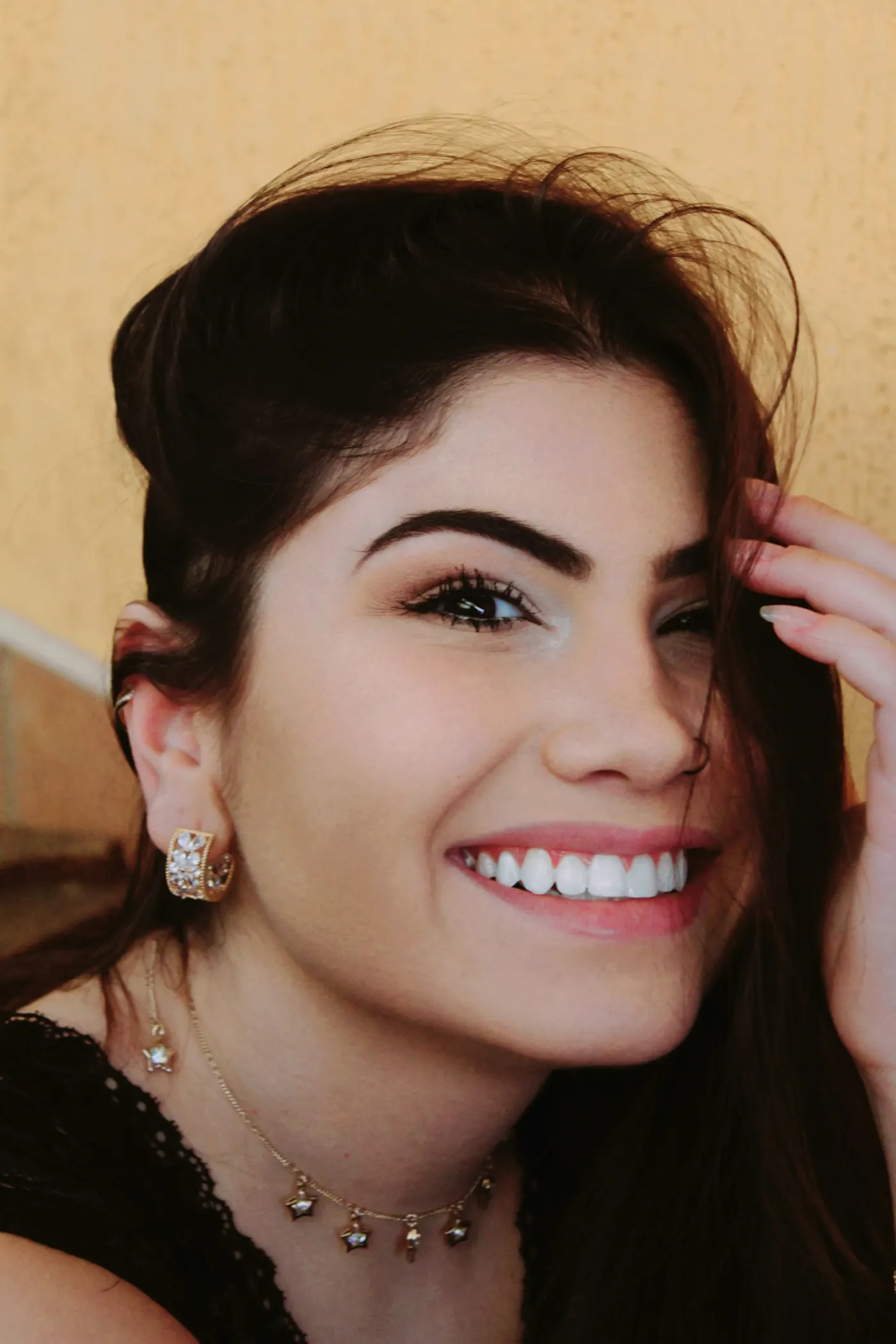 Jovem sorrindo com a mão no cabelo, sobrancelha marcada e batom rosado