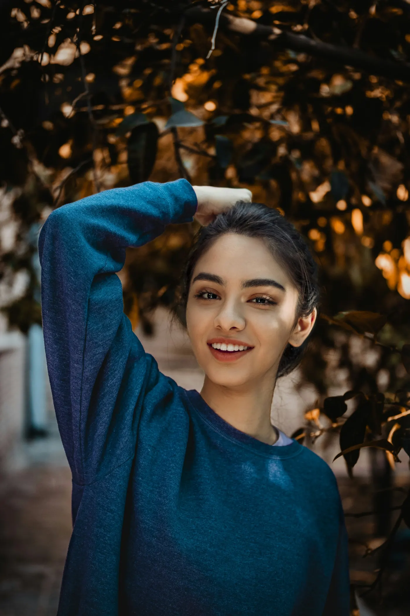Jovem de blusa azul sorrindo com o braço sobre a cabeça