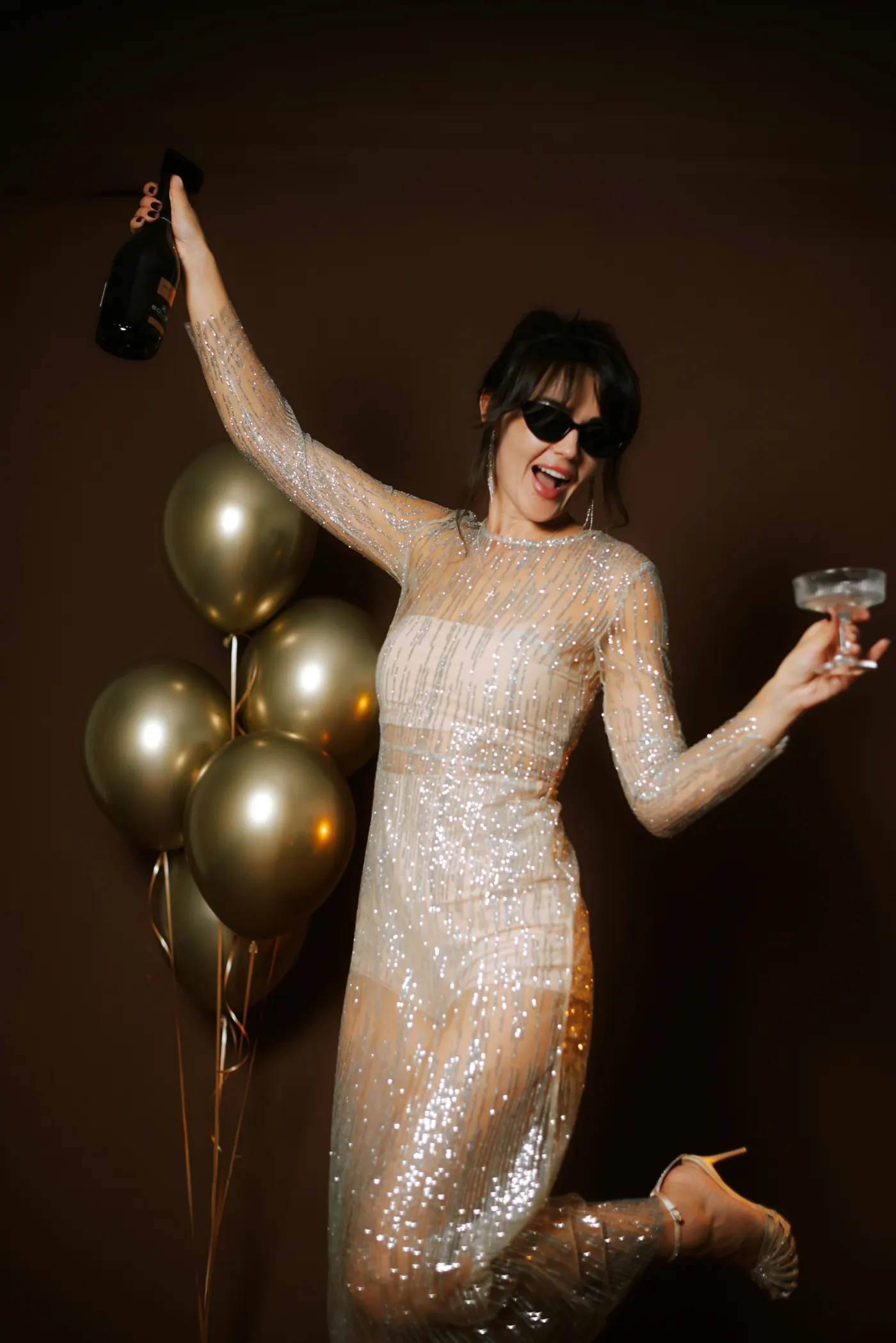 Mulher de vestido brilhante comemorando entre balões dourados