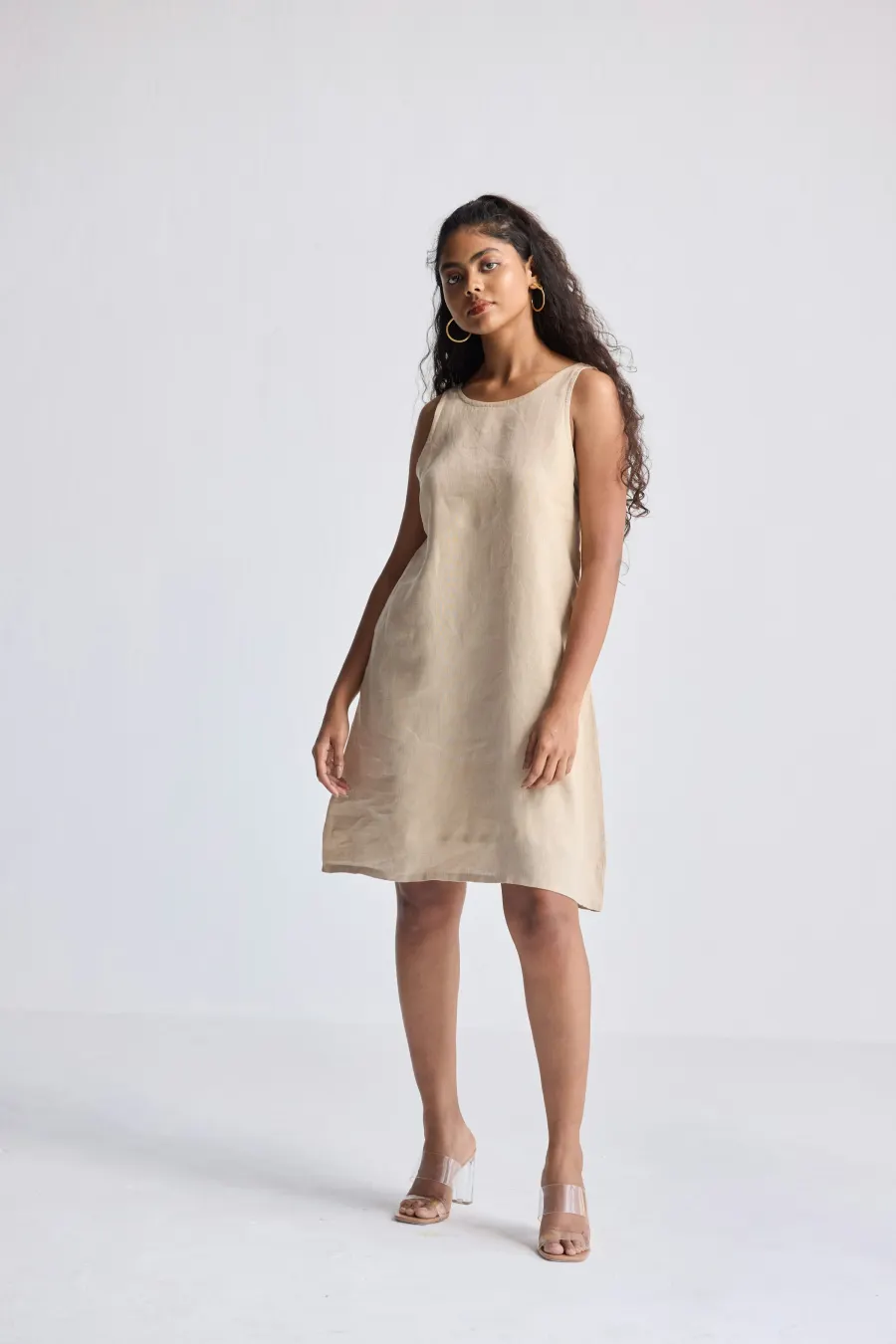 Mulher de vestido curto de linho bege cru, de pé em fundo claro
