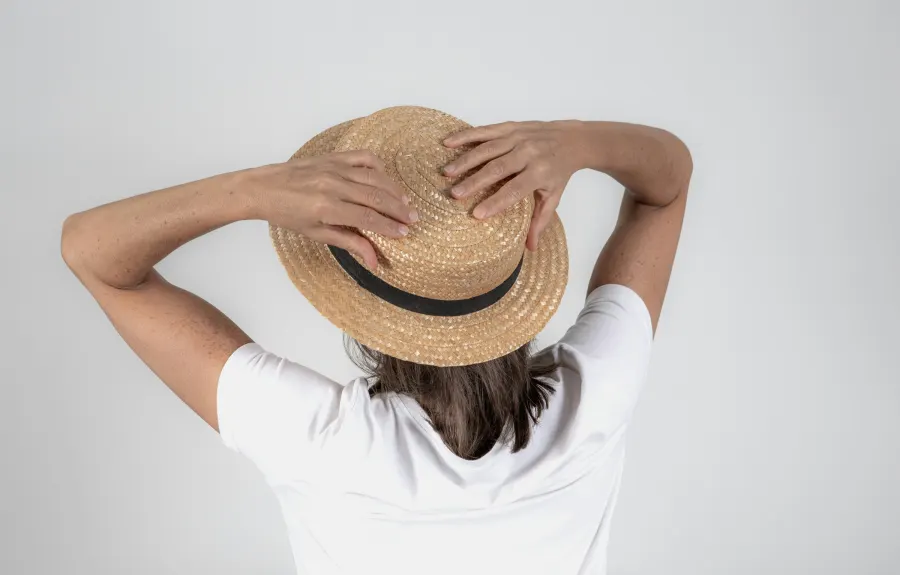 Mulher de costas segurando um chapéu de palha com fita preta
