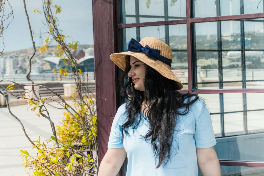 Mulher de perfil usando chapéu de palha de aba larga com laço azul