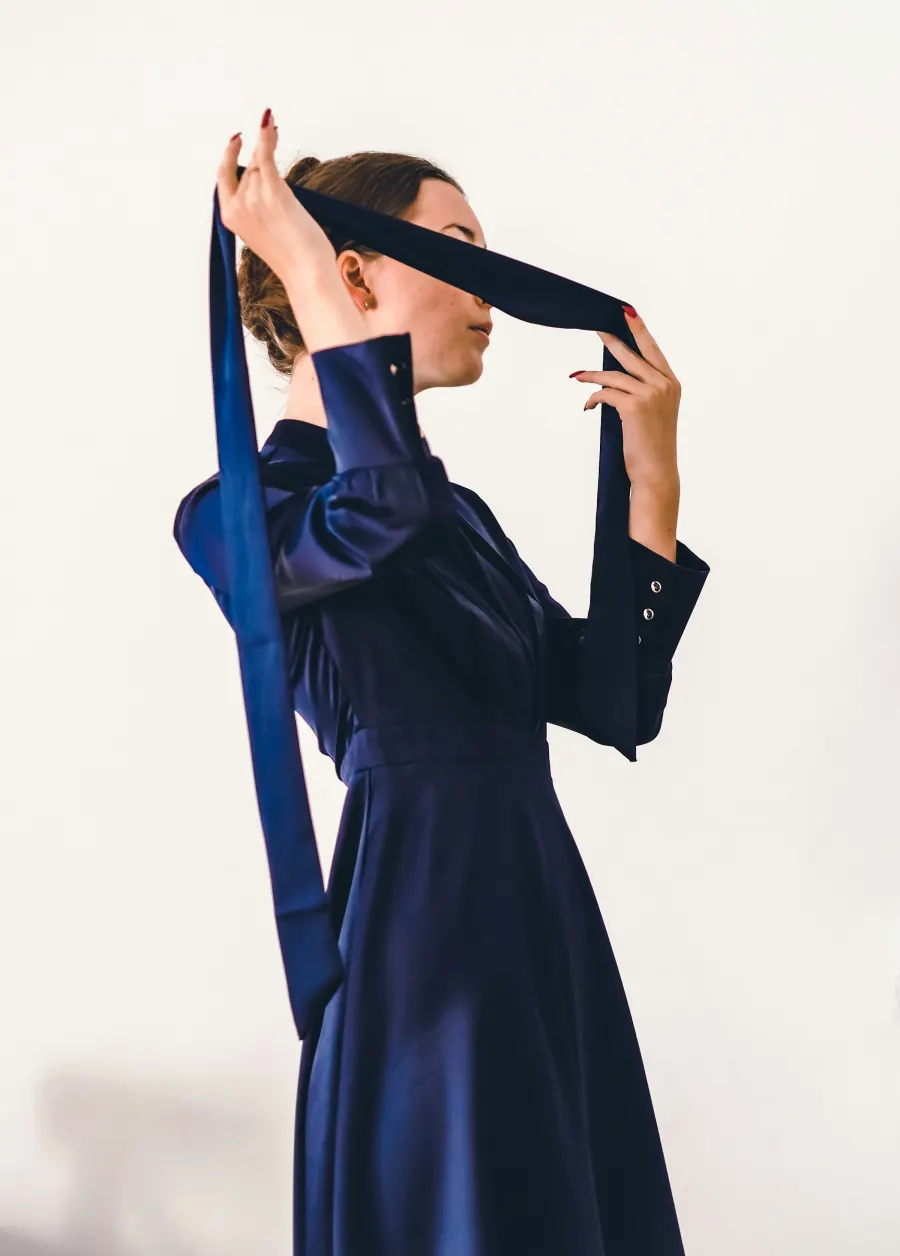 Mulher de vestido de cetim azul-marinho de manga longa, com uma fita azul diante do rosto