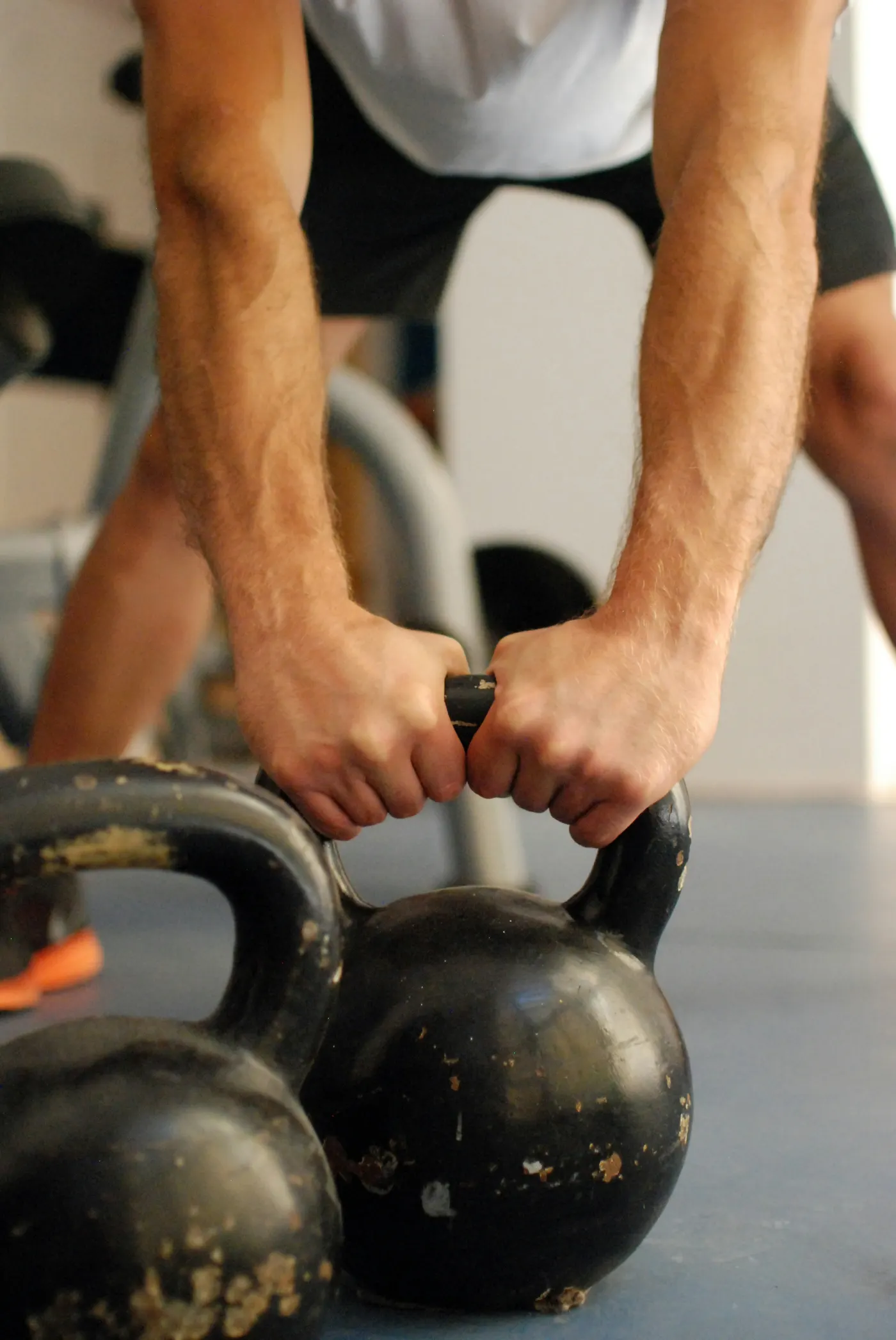 Mãos seguram a alça de dois kettlebells de ferro no chão