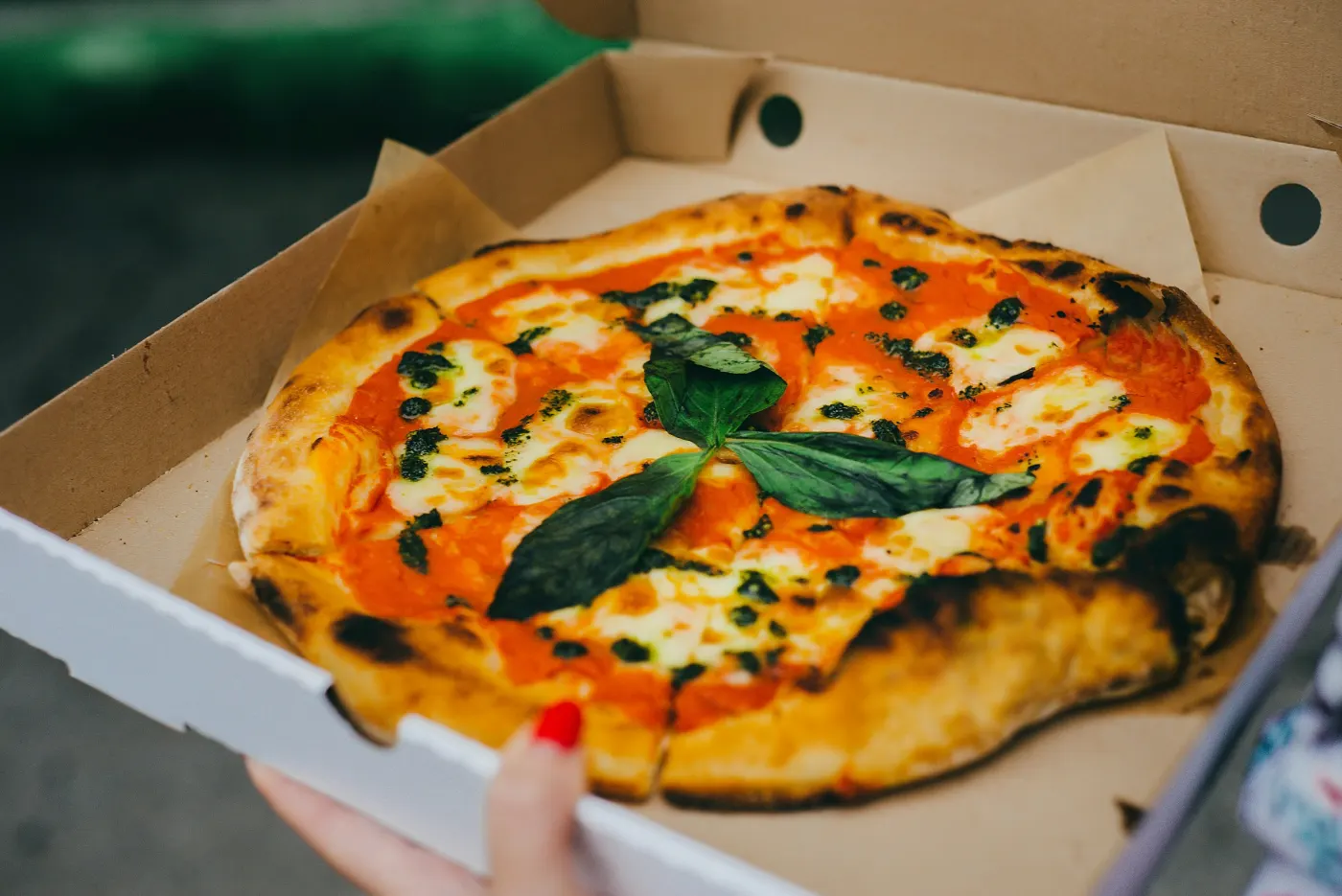 Pizza margherita de borda tostada numa caixa de entrega aberta, segurada por uma mão