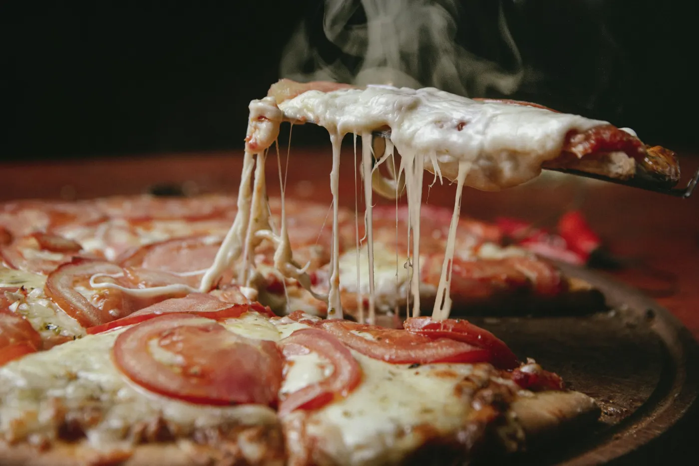 Fatia de pizza de muçarela com tomate sendo erguida, com o queijo esticando e vapor subindo