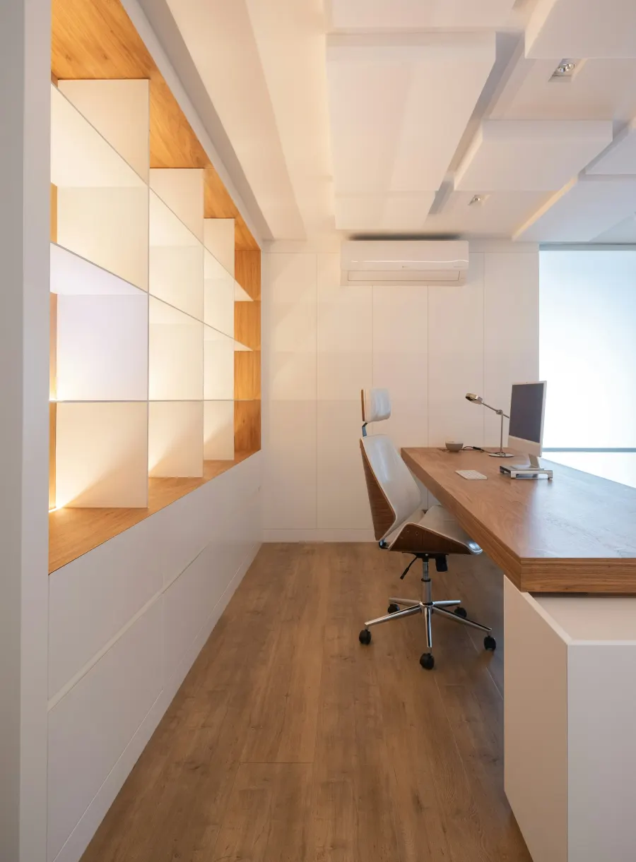 Home office com bancada de madeira, armário branco e nichos com luz embutida
