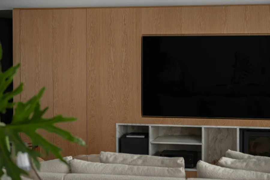 Parede da sala em madeira clara com a televisão embutida e nicho de pedra embaixo
