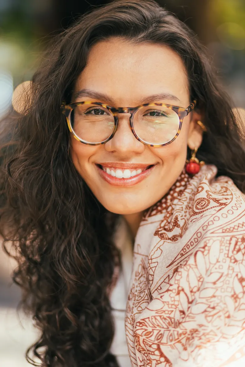 Retrato de Renata Lins, psicóloga, sorrindo, de óculos e cabelo cacheado