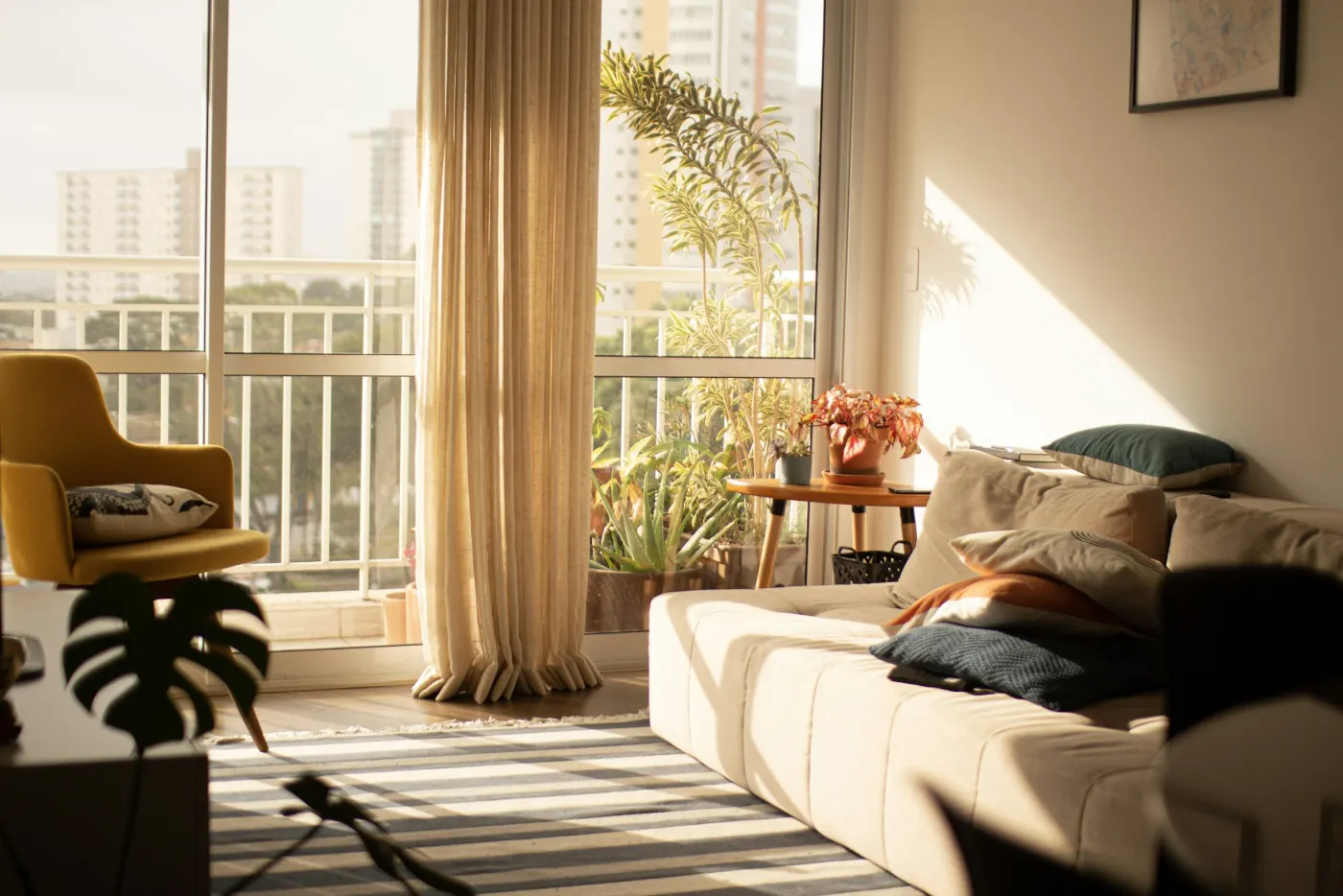 Sala de apartamento pronta, com porta de varanda, cortina de linho, sofá claro e piso de madeira